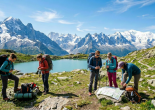 Campers at two tents near an Alpine mountain lake with snowy peaks
