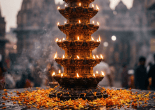 Tiered oil lamp burning among flower petals at a temple